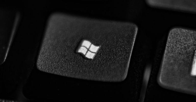 Close-up of a keyboard key with the Windows logo. The key is black and slightly textured, while the logo is white, centered on the key. The image is in grayscale, highlighting the keys design.