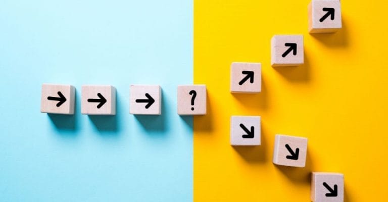 Wooden blocks with black arrows and a question mark are arranged on a split background of blue and yellow. Arrows on the left point right, leading to a question mark, while arrows on the right point upwards in a diagonal line.