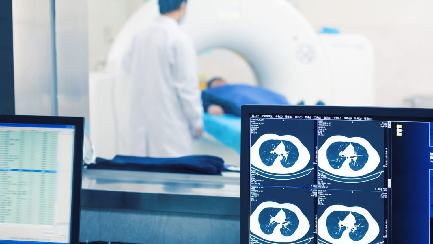 A medical professional stands next to a patient lying on a CT scanner bed, while computer monitors in the foreground display lung scan images and medical data.