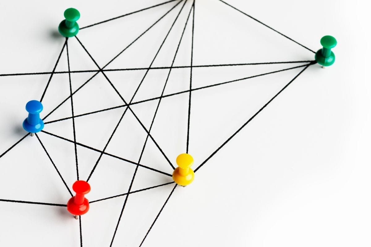 Colored push pins connected by black strings on a white background, forming a network pattern to represent interconnectedness or communication.