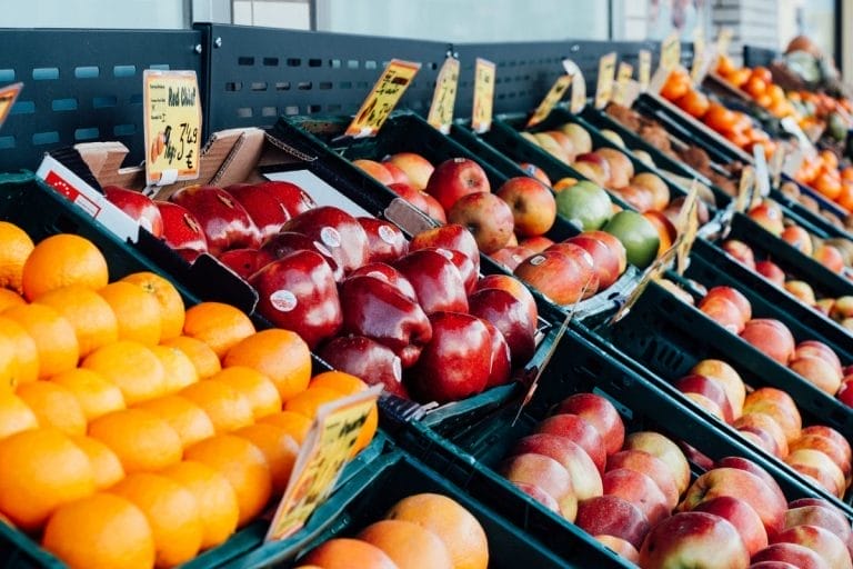 A supermarket display shows neatly arranged trays of fresh oranges, apples, mangoes, and other fruits, with price tags above each row—offering options for Raisers Edge users in 2025 who seek vibrant, organized selections.