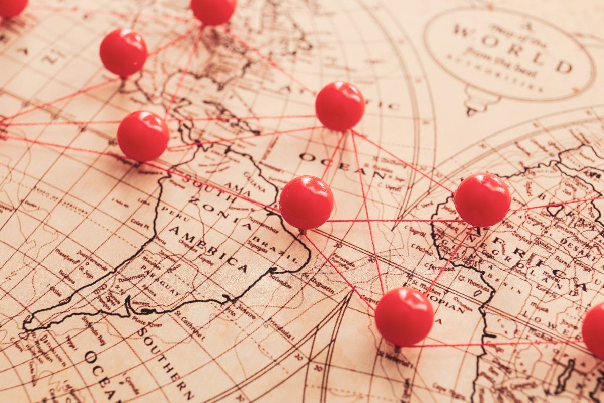 Close-up of a vintage world map with red push pins connected by red string, marking various locations across North America, Europe, and surrounding regions.