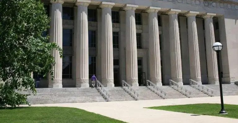 A large building with tall columns and wide steps at the entrance, flanked by a green lawn and leafy tree, stands as a symbol of nonprofit digital transformation, with a black-and-white lamppost on the right side.