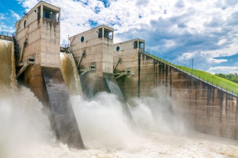 A concrete hydroelectric dam releases water through its spillways, creating mist and turbulent flow below, with blue sky and clouds overhead—much like how Nonprofit CRM costs explained helps clarify the flow of expenses for organizations.